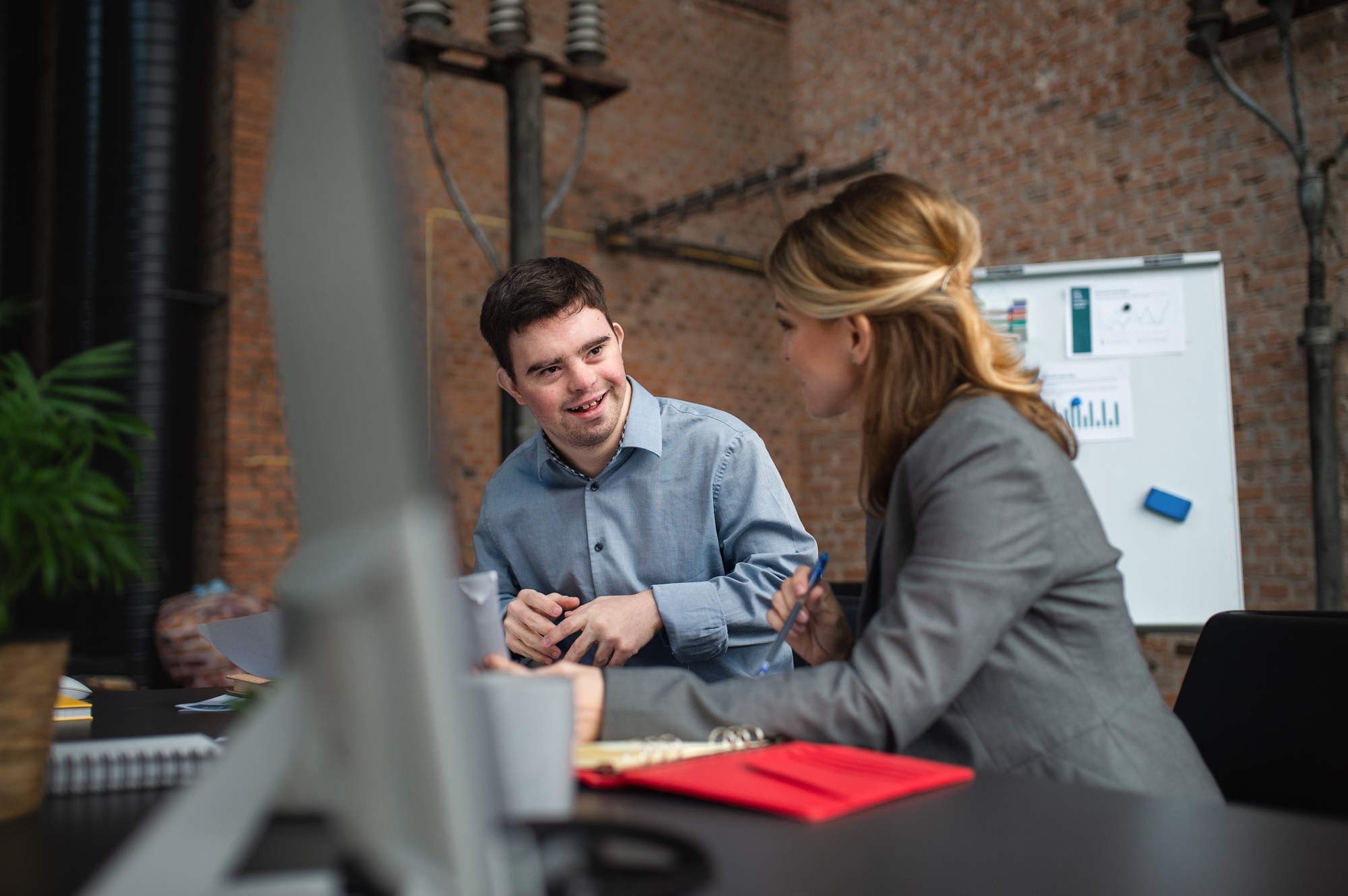 Down syndrome man with businesswoman colleague working, social inclusion and cooperation concept.